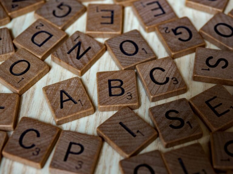 Scattered wooden Scrabble tiles showcasing letters and typography on light wooden surface.