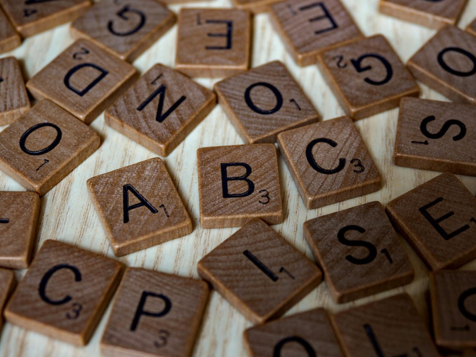 Scattered wooden Scrabble tiles showcasing letters and typography on light wooden surface.