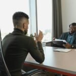 Two men in a job interview setting in a modern office with large windows.